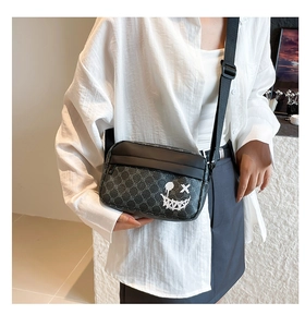 Detail of grey checkered crossbody phone bag featuring a white graffiti smiley face print
