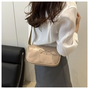 Detail of beige faux leather shoulder bag featuring a golden metal bow and wide canvas strap