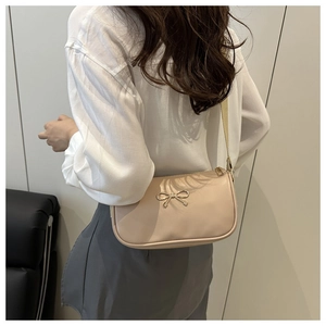 Détail d'un sac bandoulière beige en cuir avec nœud doré et large sangle d'épaule
