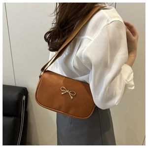 Detail of a brown PU leather crossbody bag with a gold metal bow and wide canvas strap
