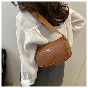Detailed shot of brown faux leather crossbody bag with golden bow and wide strap