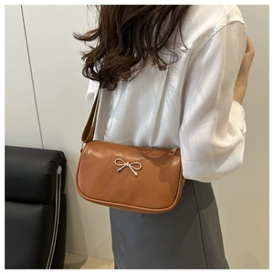 Detail of a brown leather semicircular crossbody bag with a golden metal bow ornament