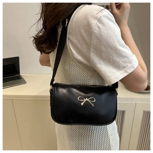 Close-up of black crossbody bag featuring a decorative gold metal bow on smooth faux leather