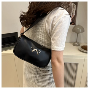 Detail of black matte shoulder bag with gold bow clasp worn by a model in lifestyle setting