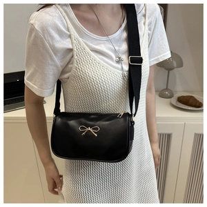 Détail d'un sac bandoulière noir avec nœud papillon doré et large sangle en nylon noir