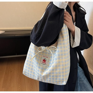 Detail of blue and yellow plaid canvas bag featuring handmade tomato logo tag and drawstring