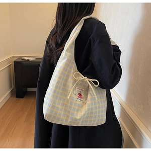 Detail of yellow and blue plaid canvas bag featuring a tomato brand label and side bow tie