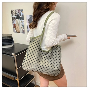 Detailed side view of a large green polka dot tote bag worn over the shoulder in a cozy room