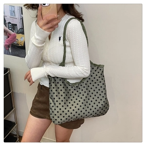 Detail of olive green tote bag with black polka dots worn on shoulder over white top