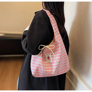 Detail of a pink and blue checkered tote bag showing the side drawstring bow and woven label