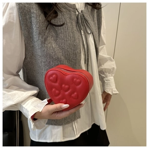 Detail of red heart-shaped leather crossbody bag with quilted patterns on a model