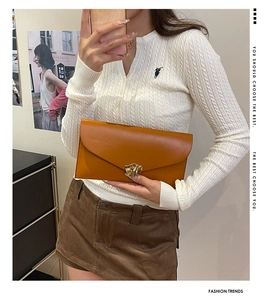 Détail d'une pochette enveloppe marron avec boucle en métal doré ondulé lors d'un selfie