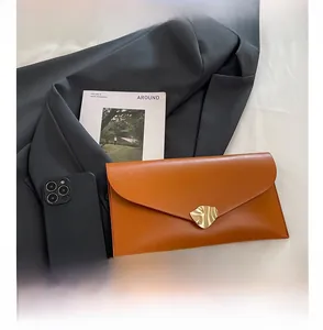 Gros plan sur une pochette enveloppe en cuir gingembre avec boucle dorée et coutures fines