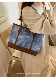 Detail of blue denim tote bag with leather straps and retro fashion logo on a shoulder