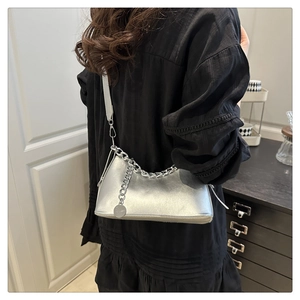 Silver leather crossbody bag featuring a chunky chain and round pendant worn with a black dress
