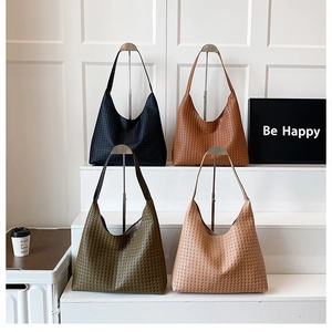 Collection of four woven leather tote bags in black, brown, green and beige displayed on stands