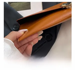 Détail d'une pochette en cuir marron montrant les coutures de précision et la boucle dorée