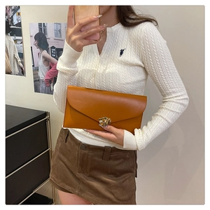 Détail d'une pochette enveloppe en cuir marron avec un fermoir en métal doré ondulé