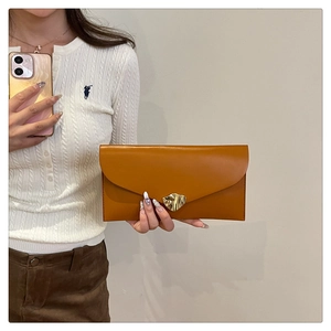 Detailed close-up of caramel leather envelope clutch with a wavy gold metal buckle