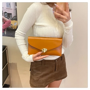 Pochette enveloppe en cuir caramel avec boucle dorée montrée lors d'un selfie miroir