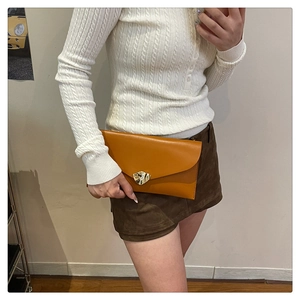 Détail du sac enveloppe orange-brun avec élégante boucle en métal doré en forme d'onde