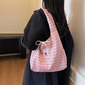 Pink and blue plaid tote bag with drawstrings shown on model in a minimalist setting