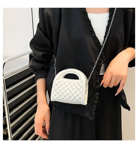 Detail of white quilted handbag with silver chain strap and top handle on a person