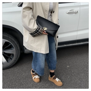 Pochette enveloppe noire élégante avec boucle feuille dorée et trench-coat beige