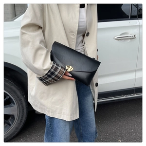 Détail d'une pochette enveloppe en cuir noir avec boucle cœur dorée devant une voiture