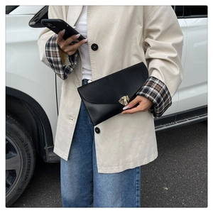 Detail of a black leather envelope clutch with a gold geometric metal magnetic closure