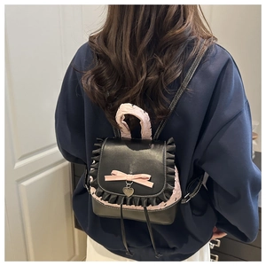 Detail of mini black leather backpack with pink bow, lace trim and heart charm on model