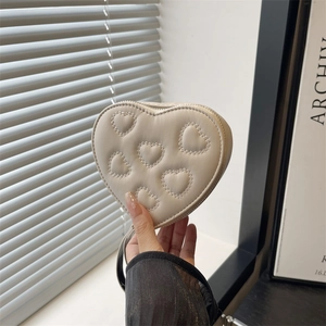 Chic cream heart-shaped quilted mini clutch bag held by hand in a minimalist interior