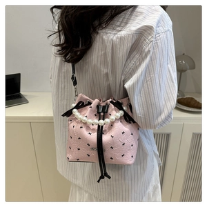 Detail of pink bucket bag with black bows, pearl handle and adjustable crossbody strap
