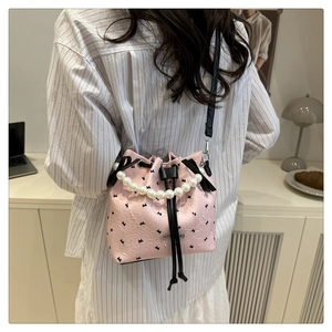 Detail of pink bucket bag with pearl handle and bow patterns worn by a model in a room