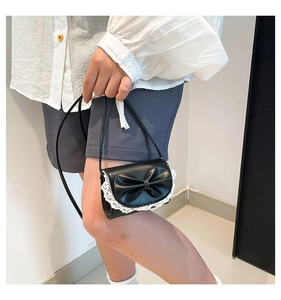 Detail of sweet black mini crossbody bag with a large bow and white lace trim detail