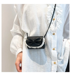 Close-up of black mini crossbody bag with large bow and white lace trim detail