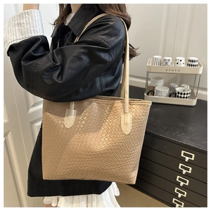 Woven leather tote bag in beige shown on shoulder with black leather jacket detail