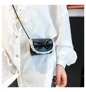 Close-up of black crossbody bag with decorative bow and white lace trim detail