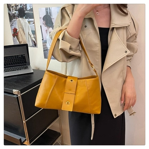 Detail of a vintage ginger yellow faux leather shoulder bag worn by a model in a city scene