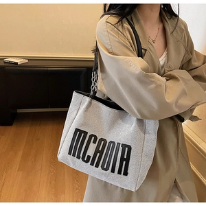 Detail of grey canvas tote bag with embroidered letters and chain link shoulder strap