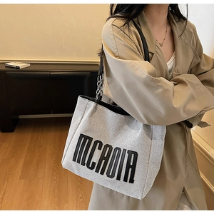 Detail of grey canvas tote bag with black letter print and metal chain leather strap