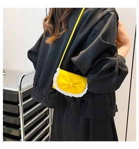 Detail of bright yellow crossbody bag with large bow and white lace trim detail