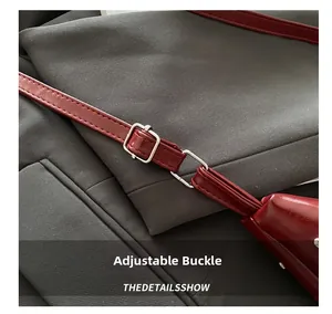 Detail of adjustable silver metal buckle on wine red faux leather strap of handbag