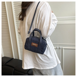 Detail of dark blue denim pillow bag with white contrast stitching and adjustable strap