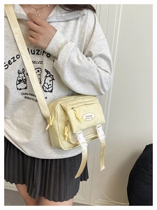 Detail of light yellow nylon crossbody bag with dual buckles on a female model