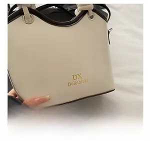 Detail of cream bucket bag showing DX logo, smooth leather texture and contrast edge