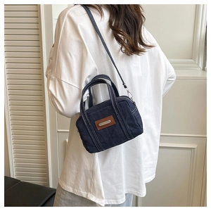 Detailed close-up of dark blue denim handbag with white stitching and leather patch