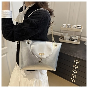 Detail of silver tote bag with golden deer charm and elegant chain strap on shoulder