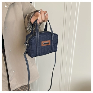Detail view of denim pillow bag with contrast stitching and brown leather patch