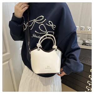 Detail of white bucket bag with coffee trim and gold lettering on a shoulder strap